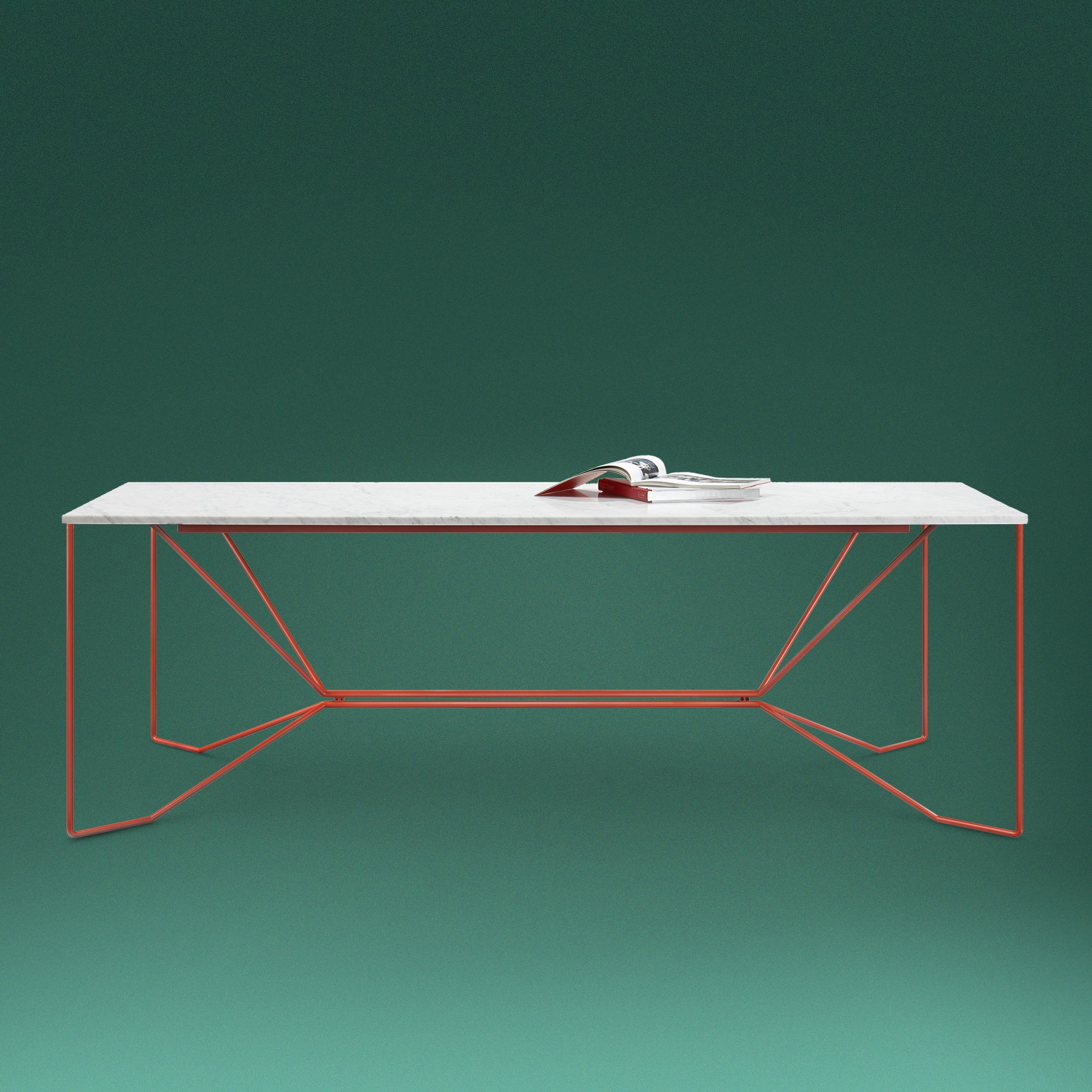 The Victor Foxtrot SAME SAME Marble Table, with a pristine Carrara Venatino marble top and bold geometric powder-coated steel legs, stands against a dark green background. An open book adds a minimalist touch to its sleek design.