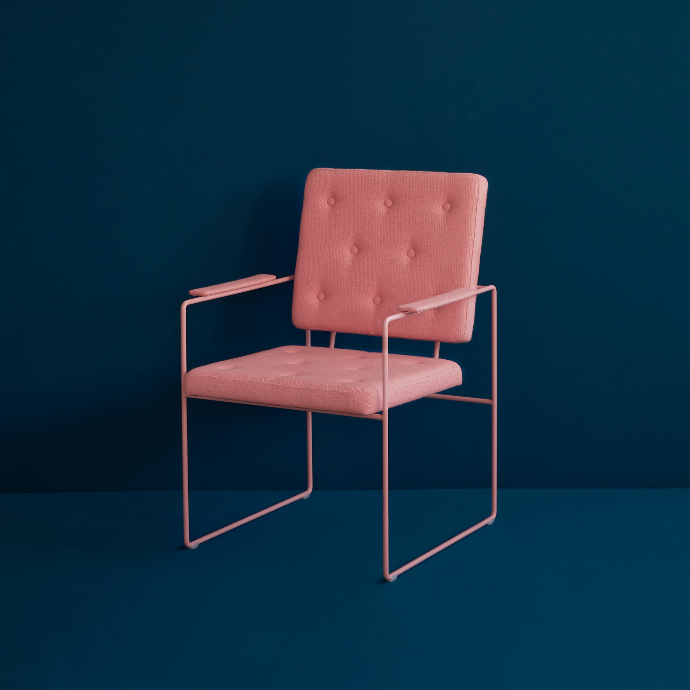 The SWELL TIME Dining Chair by Victor Foxtrot features a pink cushioned seat and backrest with button stitching, set against its minimalist steel frame. The chairs contrast with the dark teal background creates a striking visual impact.