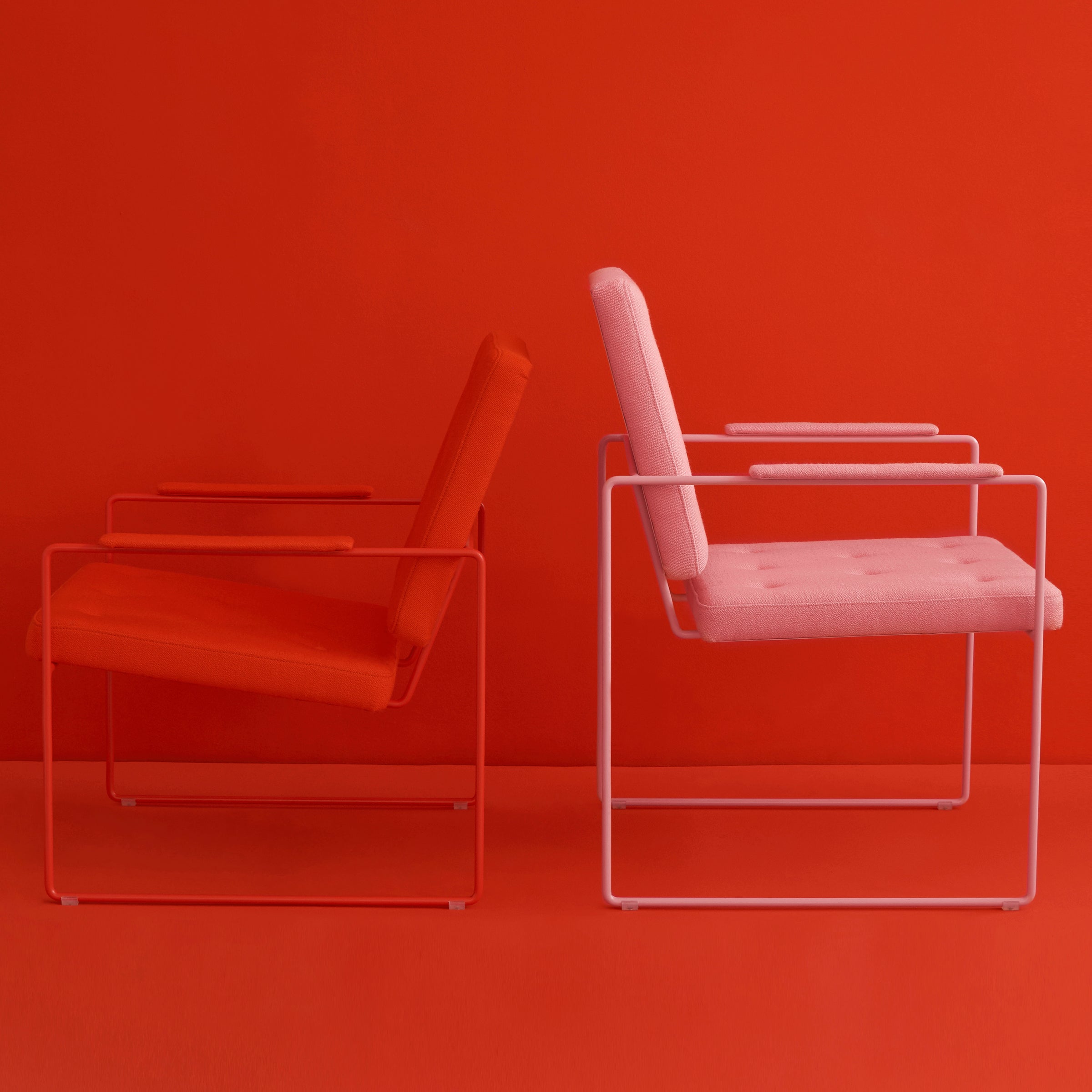 Two SWELL TIME Dining Chairs by Victor Foxtrot are set against a bold red backdrop. The left chair is deep red, the right is soft pink, offering striking contrast. Elegant button stitching details highlight each chairs modern design with steel frames.