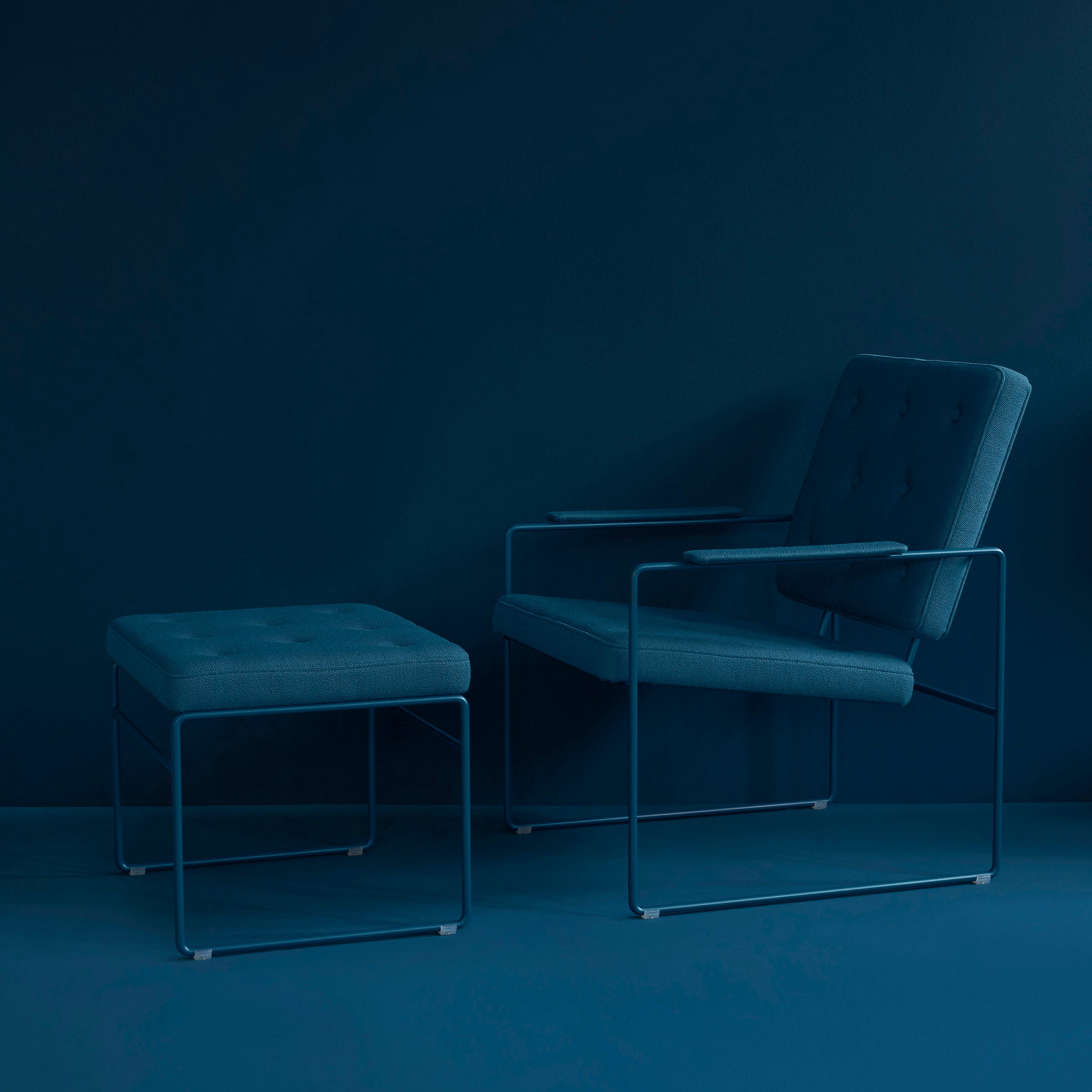 The Victor Foxtrot SWELL TIME Ottoman, with its steel frame and button-stitched cushioned seats, combines with a modern armchair against a dark teal backdrop, achieving a cohesive monochromatic look.