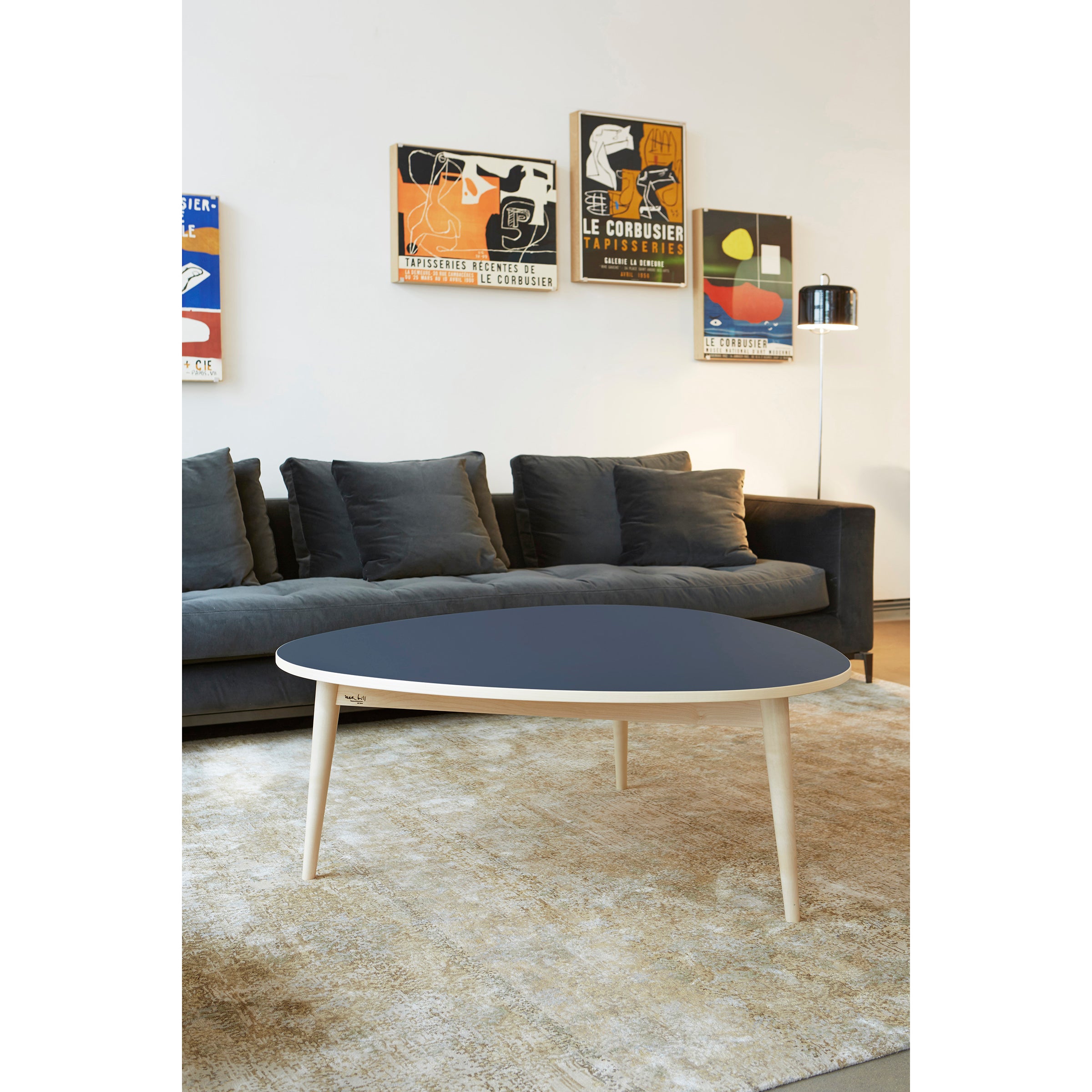 A modern living room showcases a dark gray sofa and the WB Form Drei-Rund Coffee Table on a light rug. Colorful abstract art pieces echoing geometric designs adorn the white wall. Beside the sofa, a floor lamp provides ambient lighting.