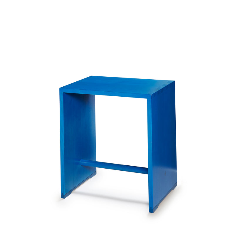 The WB Form Ulmer Stool is a minimalist blue side table with a rectangular top, open sides, and horizontal support bar near the base. reminiscent of Max Bills design, its versatile style suits any setting on a plain white background.
