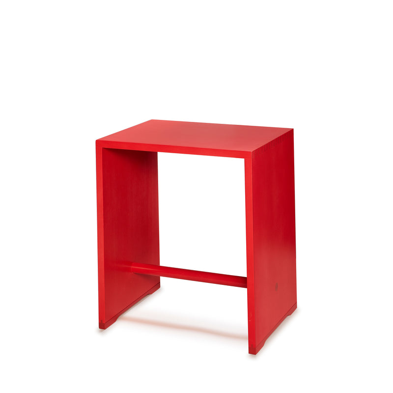 A modern red side table by WB Form, resembling the Ulmer Stool, stands out on a white backdrop. It has a rectangular top, open sides, and a horizontal base support bar. This stylish minimalist piece is offered in nine finishes.