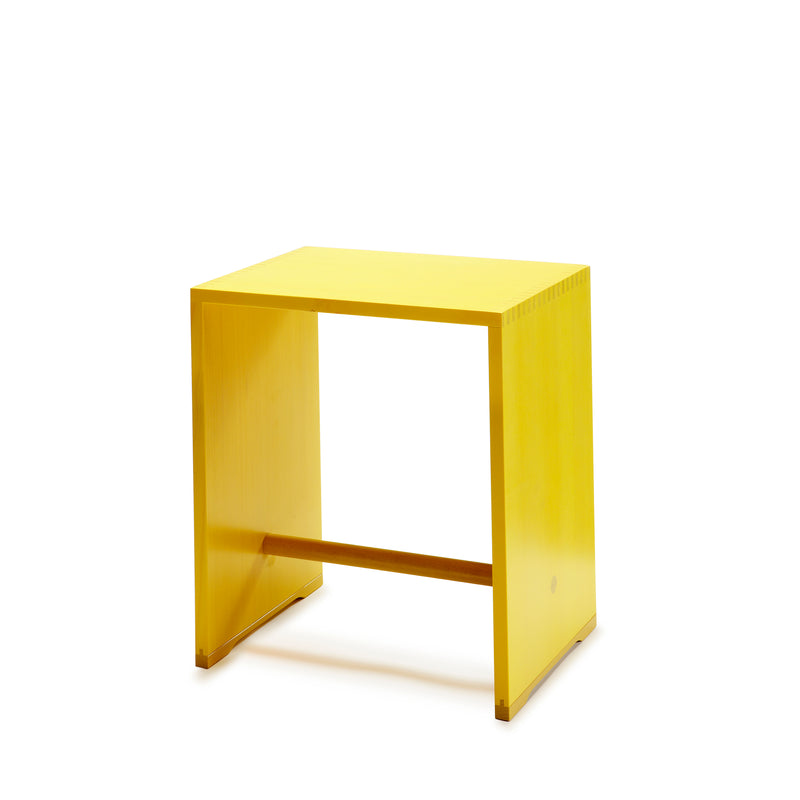 The minimalist Ulmer Stool by WB Form is a versatile yellow wooden piece with clean lines, a rectangular shape, flat top, two side panels, and a horizontal support bar near the base. Available in nine finishes, its ideal for any modern space.