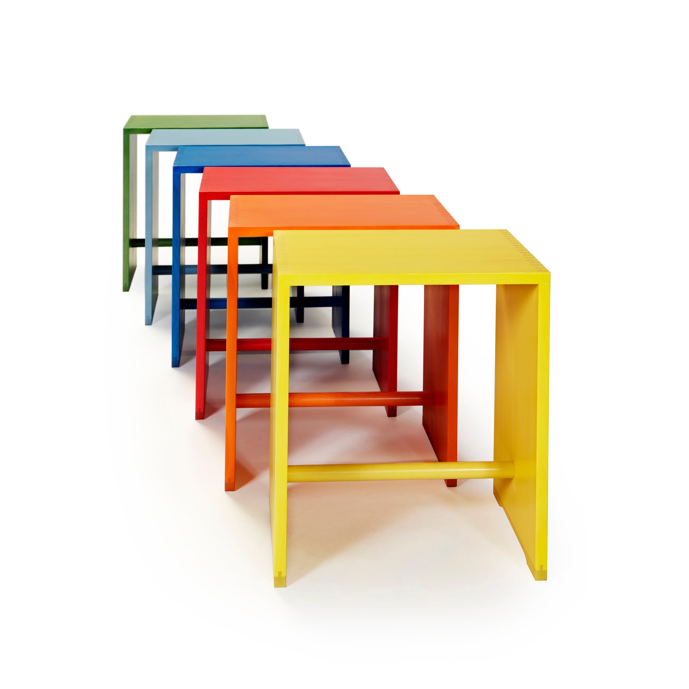 Five colorful WB Form Ulmer Stools arranged diagonally in vibrant hues of yellow, orange, red, blue, and green against a white background; these versatile stools bring a dynamic touch to any space.