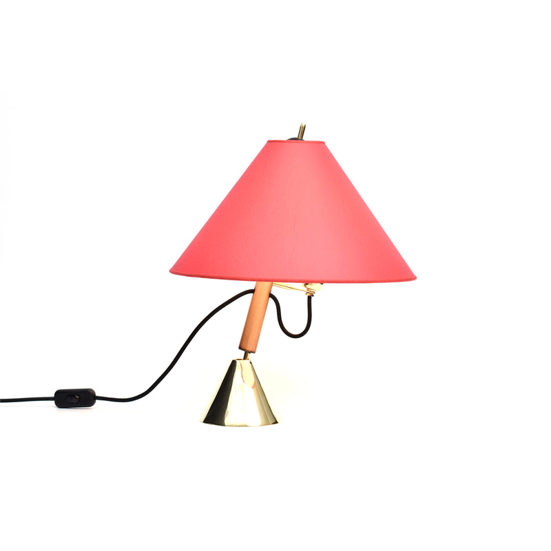 The Table Lamp Bell #3875 by Werkstätte Carl Auböck features a red, cone-shaped shade, a wooden stem, and a metallic base, capturing the elegance of a Viennese townhouse. It includes a black power cord with switch and is displayed against a plain white background.