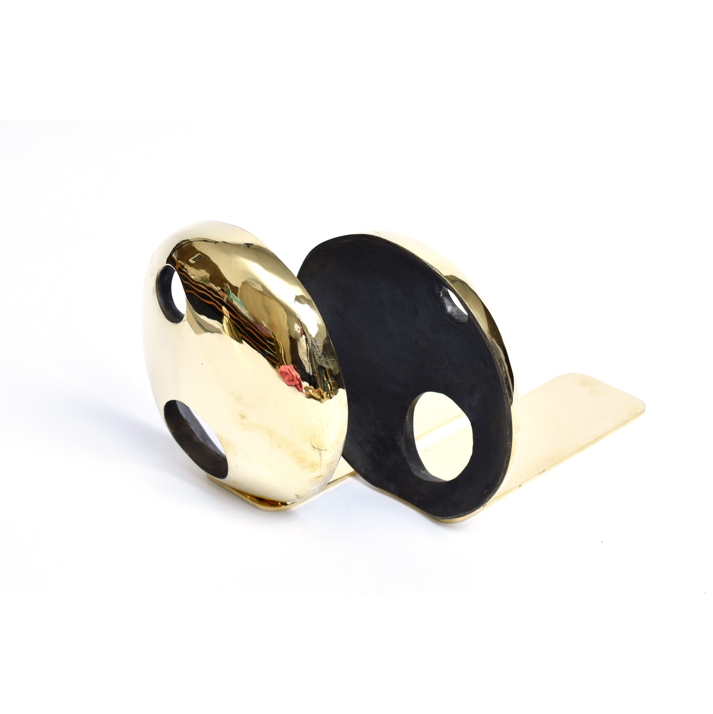 The Pair of Bookends Melies #4101 from Werkstätte Carl Auböck, with its polished gold and black finish and two round, curved shapes featuring small holes, evokes Wiener Bronzen elegance against a plain white background.