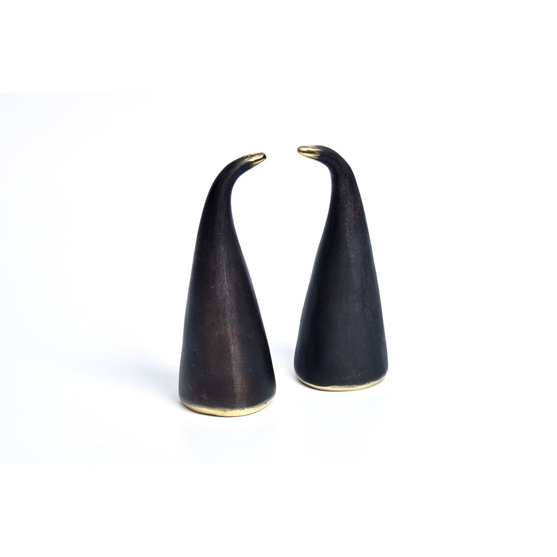 The Pair of Bookends Spectator #4102 by Werkstätte Carl Auböck features two black cone-shaped objects with an upward curve and gold accents at the base, echoing Triennale di Milano 1954 style against a plain white background. Their smooth, reflective surface recalls Auböcks iconic designs.
