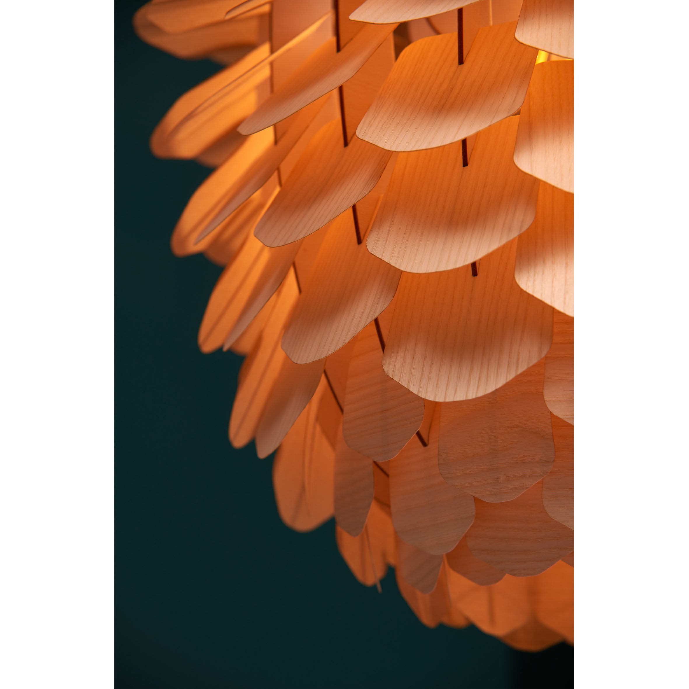 A close-up of the Zappy Ash lamp by Schneid showcases its handmade, petal-like oak veneer layers. The soft, orange glow highlights the woods texture against a dark backdrop, creating a beautiful contrast.