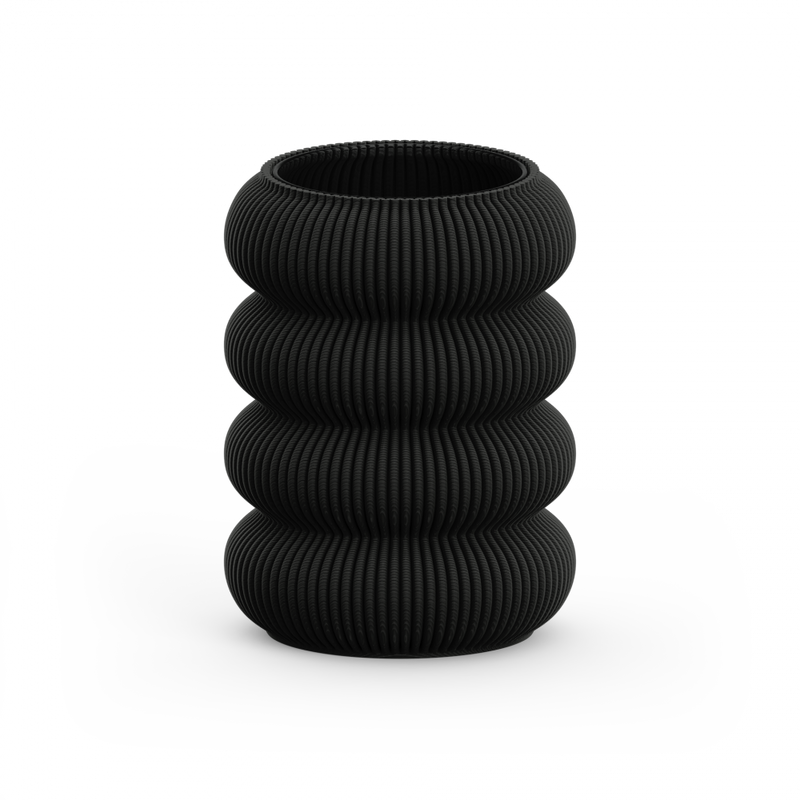 The Zayl 130g Vase by Sheyn is a black, cylindrical piece with a textured, ribbed design similar to architectural pillars. It features four stacked, rounded segments and is showcased against a plain white background.