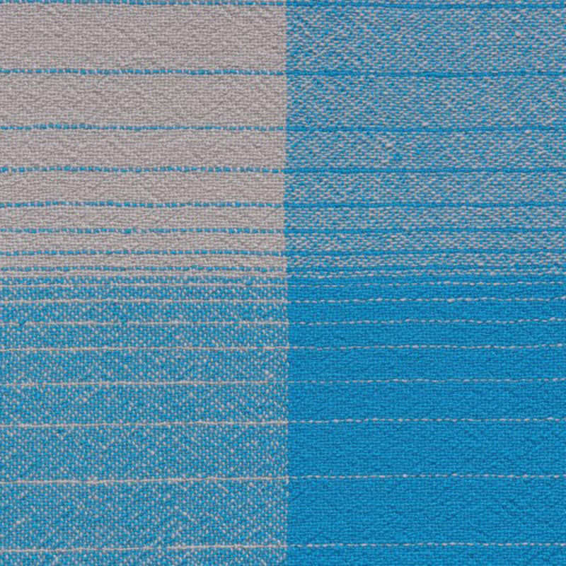 A close-up of the AC13 CUADRO blanket by E15 shows its hand-woven design: the left section is light grey with slim blue stripes, while the right is vibrant blue with fine horizontal lines, showcasing a refined texture and color contrast in merino wool.