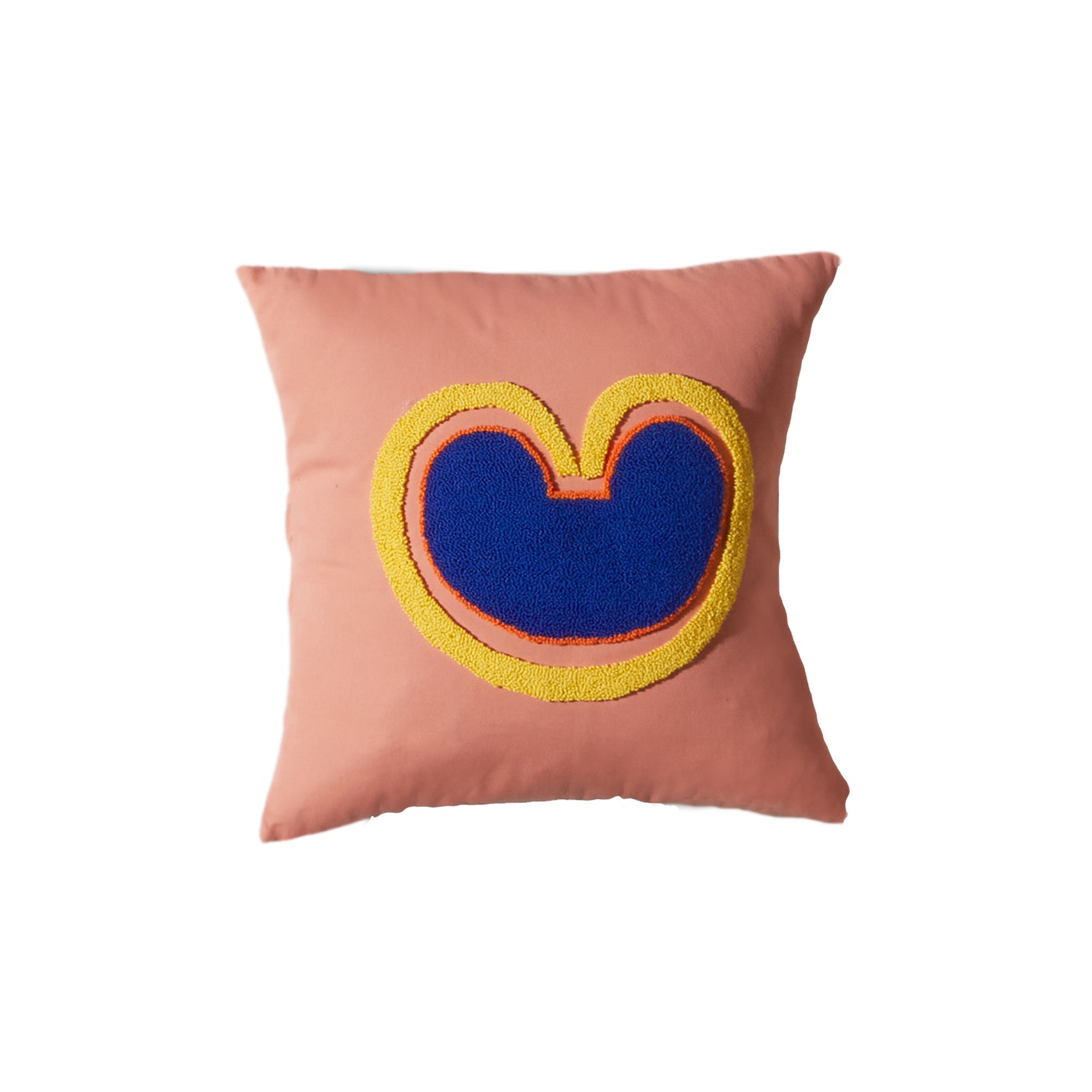 The Ames Nido Coraz cushion is a square pink pillow featuring a handmade abstract design with a blue shape outlined in yellow and orange, resembling a stylized heart or rounded M.