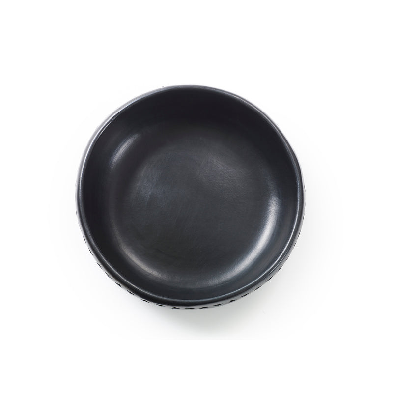 The Barro Bowl by Ames is a round, black ceramic piece with a smooth interior and slightly textured exterior, showcasing traditional pottery artistry. Photographed from above on a white background, this handcrafted bowl highlights the beauty of ceramics.