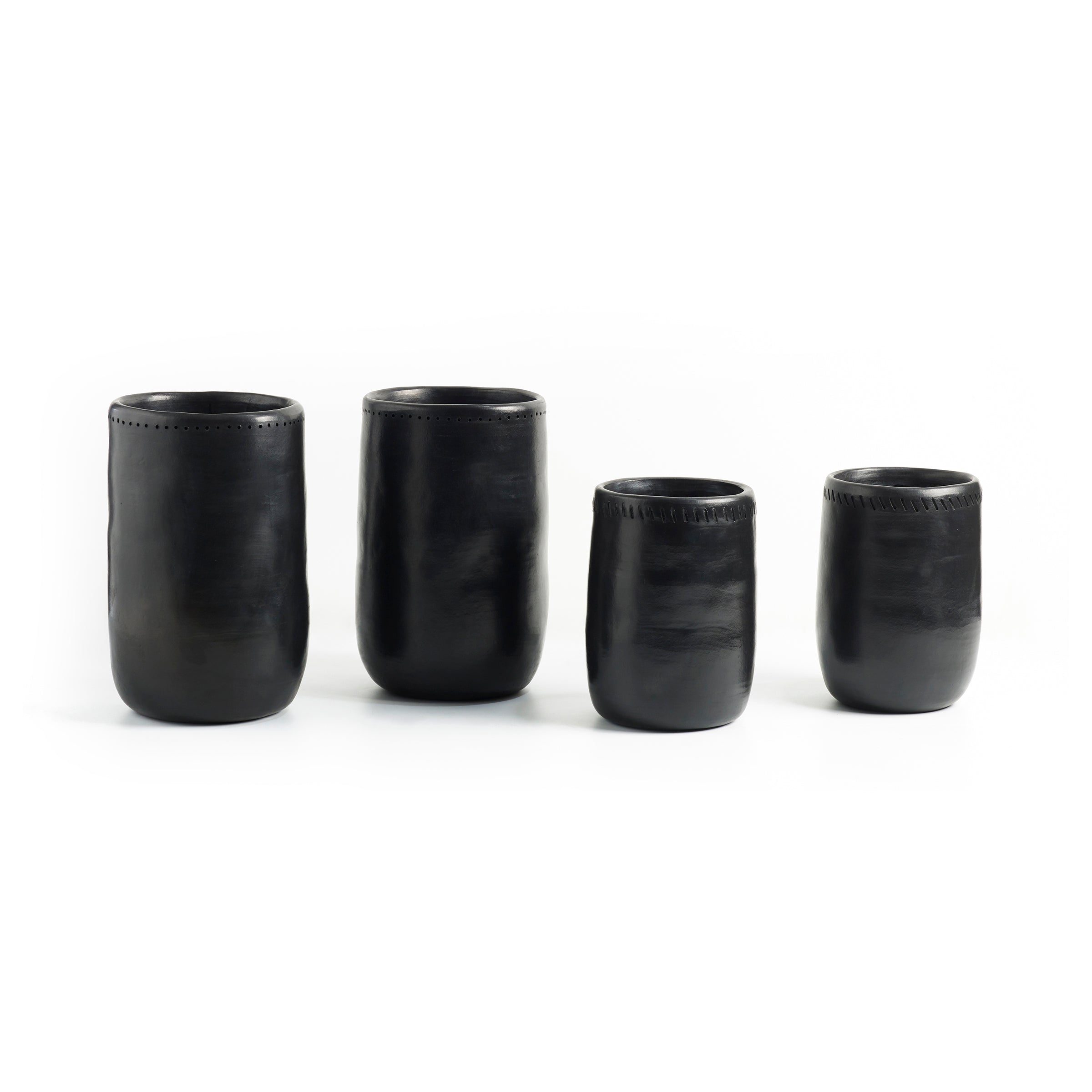 Four black Barro Vases 1 by Ames, crafted in Colombia with a smooth texture and slightly rounded shape, are arranged side by side against a white background. These vases feature simple, elegant designs and varying heights.