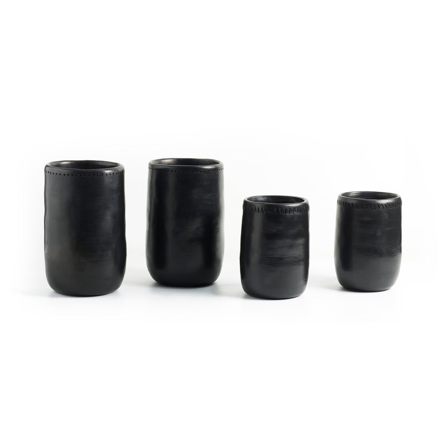 Four black Barro Vases 1 by Ames, crafted in Colombia with a smooth texture and slightly rounded shape, are arranged side by side against a white background. These vases feature simple, elegant designs and varying heights.
