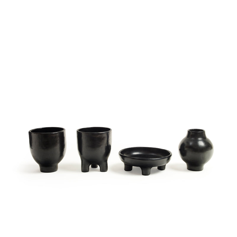 Explore the beauty of Colombian pottery with Ames: two black Barro Pot 2 cups on short legs, a three-legged shallow dish, and a small rounded vase.
