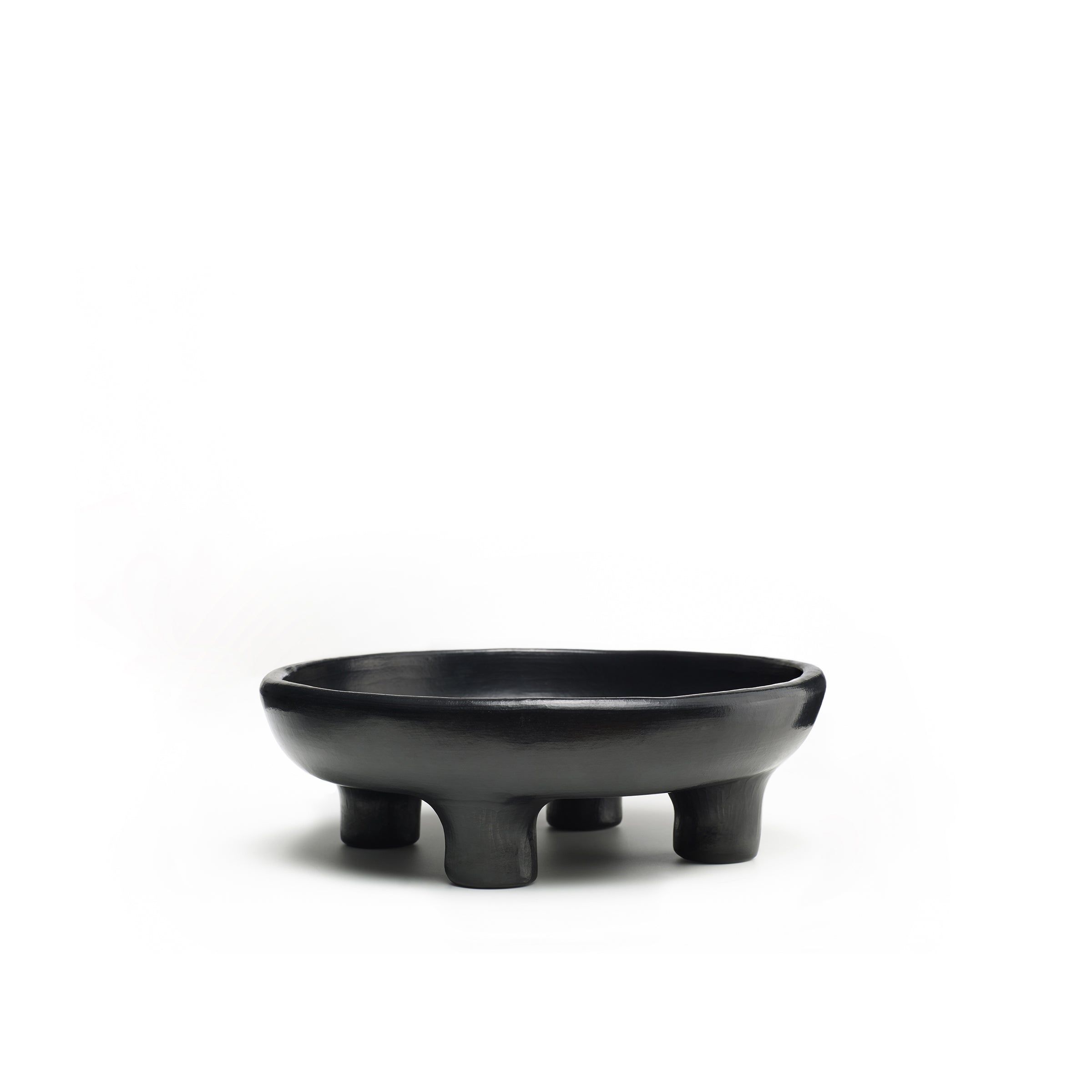 The Ames Barro Tray 1 by Ames is a black, round ceramic bowl with four sturdy legs, inspired by traditional pottery, shown against a white background.