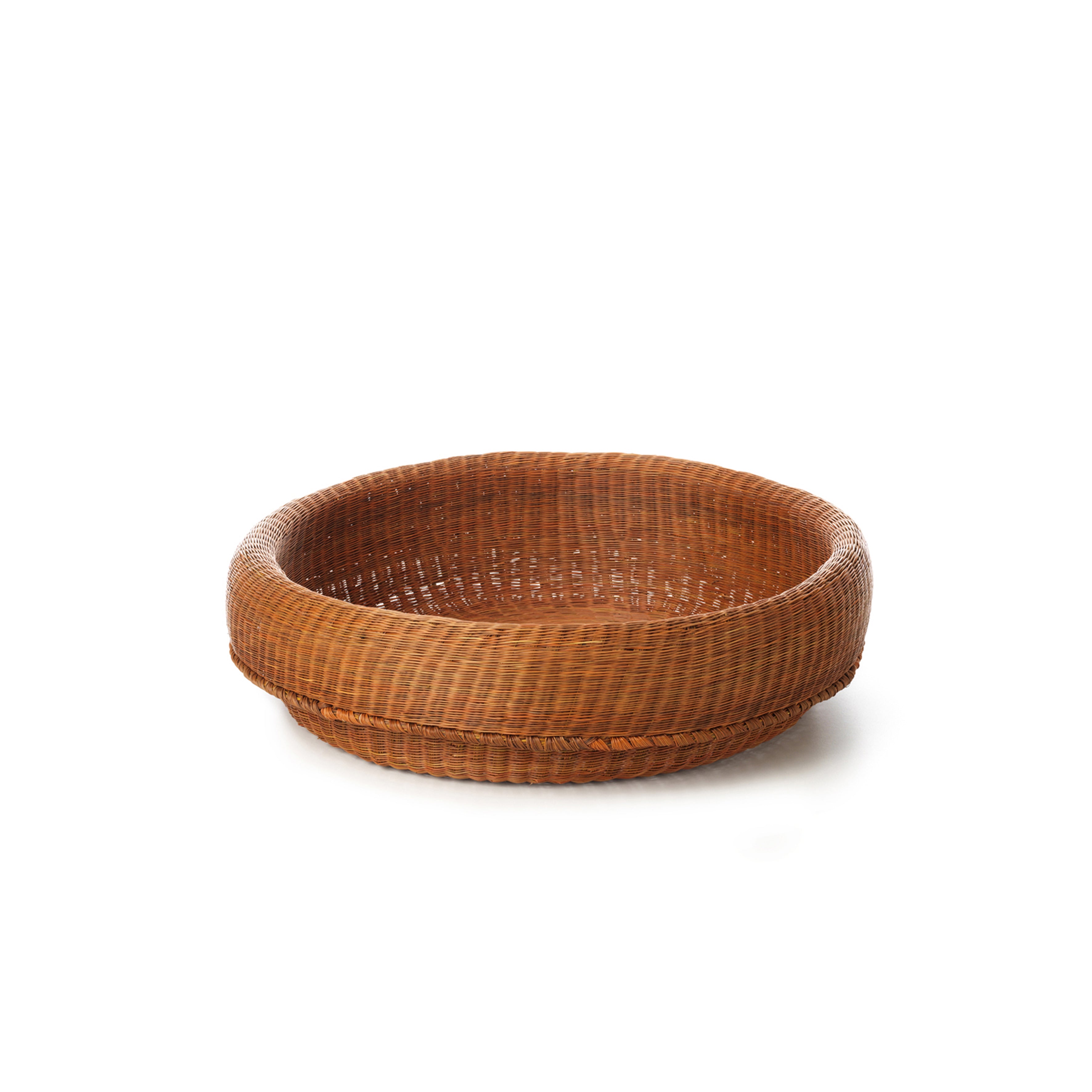 The Fibra Basket Medium by Ames is a handcrafted round wicker basket made in Colombia using esparto grass, featuring a thick woven rim. It beautifully contrasts against a white background.