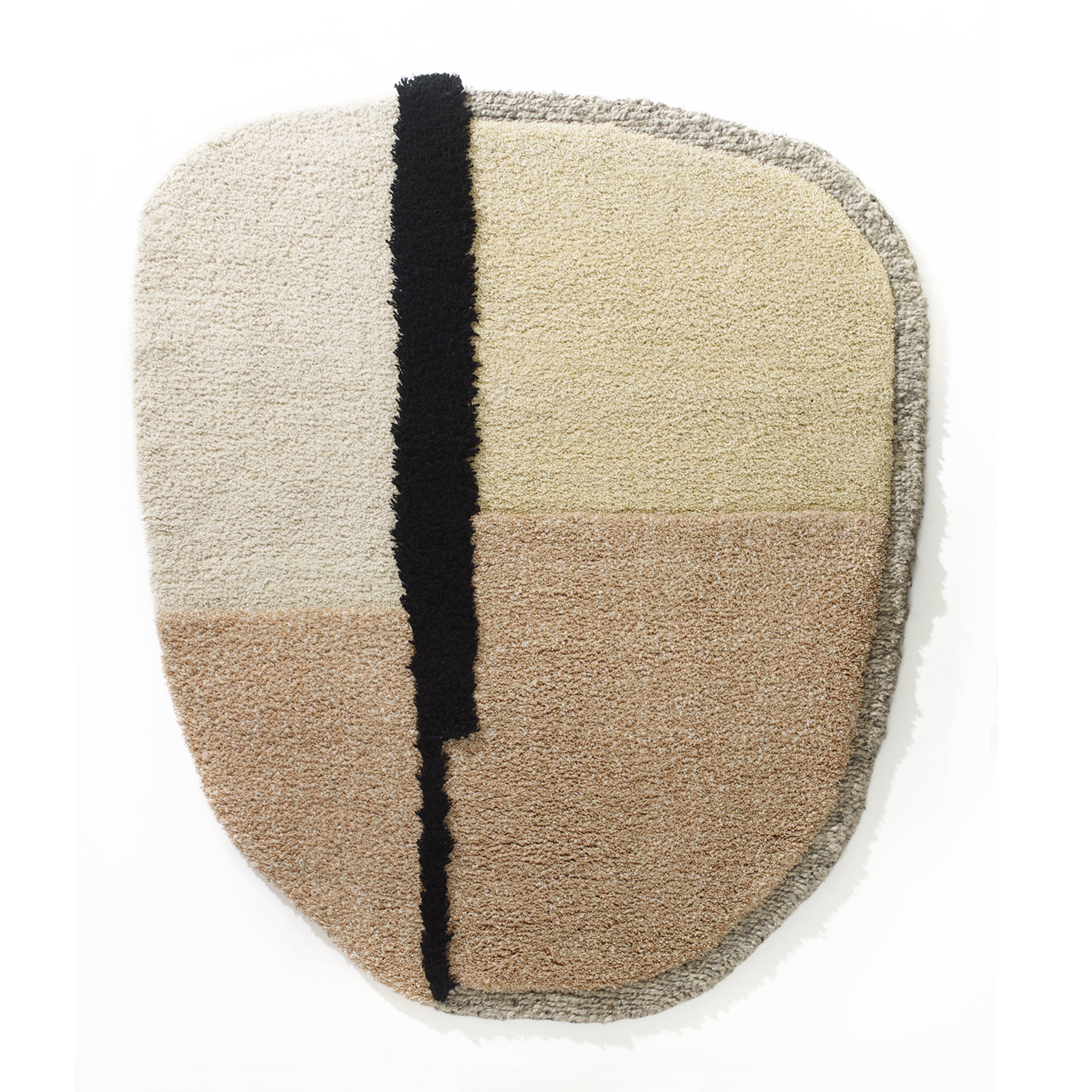 The Nudo Rug by Ames showcases a Colombian arts-inspired abstract oval design with a black vertical stripe dividing off-white, beige, and tan sections, all framed by a textured gray border.