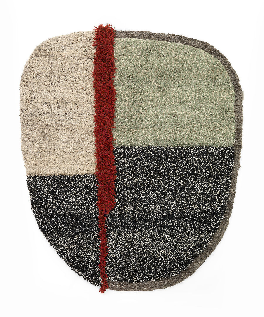 The Nudo Rug by Ames features an abstract design with an irregular shape, divided into light beige, dark speckled gray, and green sections. A red shaggy vertical strip runs off-center, bordered thinly in gray, reflecting the vibrant tradition of Colombian crafts.