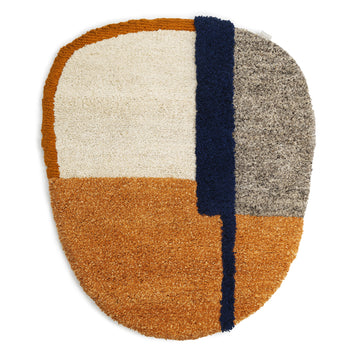 The Nudo Rug by Ames features an abstract oval design with white, gray, orange, and navy color blocks. Inspired by Colombian arts and crafts, it has a blue strip creating a modern geometric pattern. Its deep-pile texture offers exceptional softness and plush comfort.