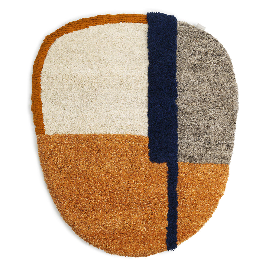 The Nudo Rug by Ames features an abstract oval design with white, gray, orange, and navy color blocks. Inspired by Colombian arts and crafts, it has a blue strip creating a modern geometric pattern. Its deep-pile texture offers exceptional softness and plush comfort.