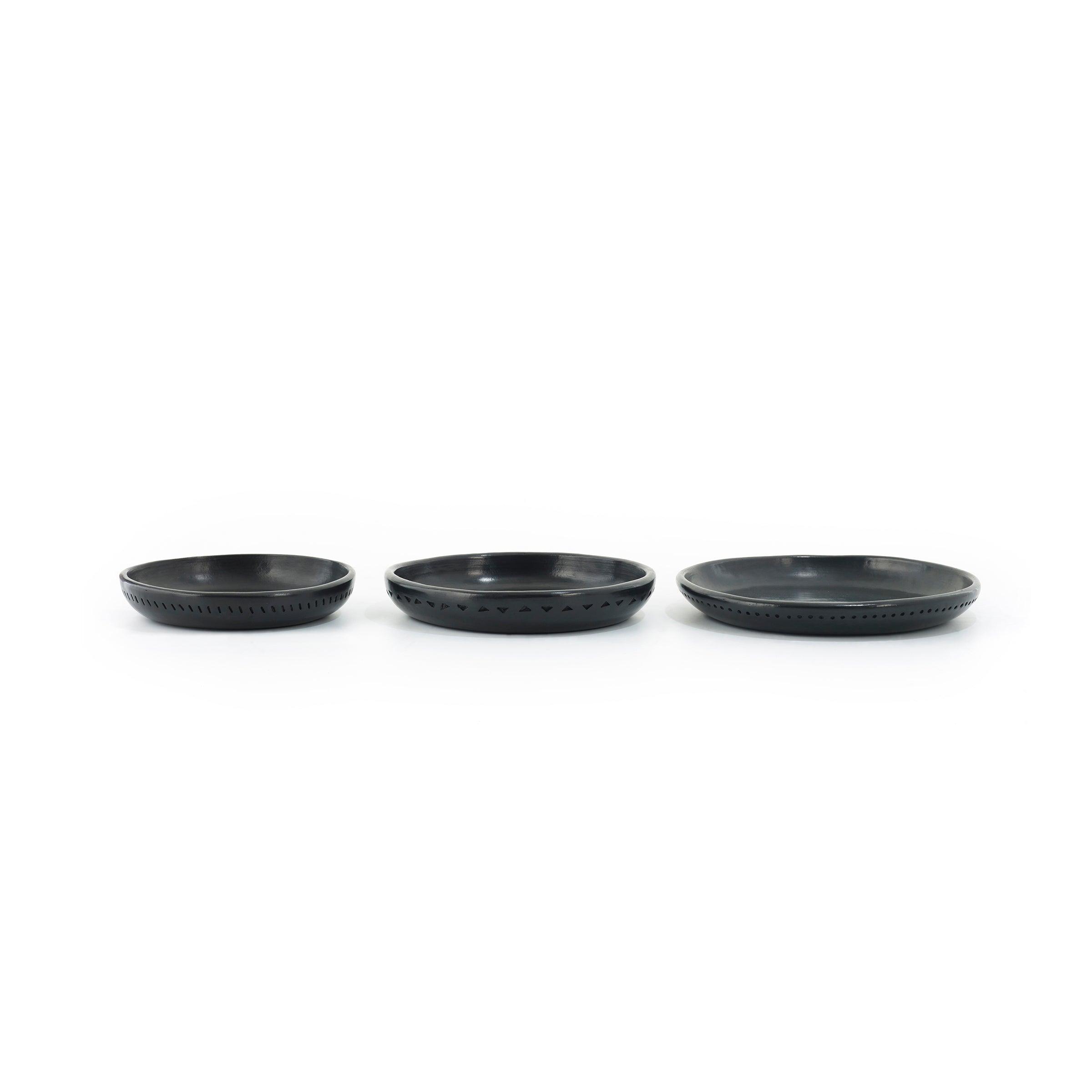 Three black, round Barro Plates of varying sizes by Ames are aligned horizontally against a white background, each crafted as unique ceramics with subtle, uniform patterns around the rim.