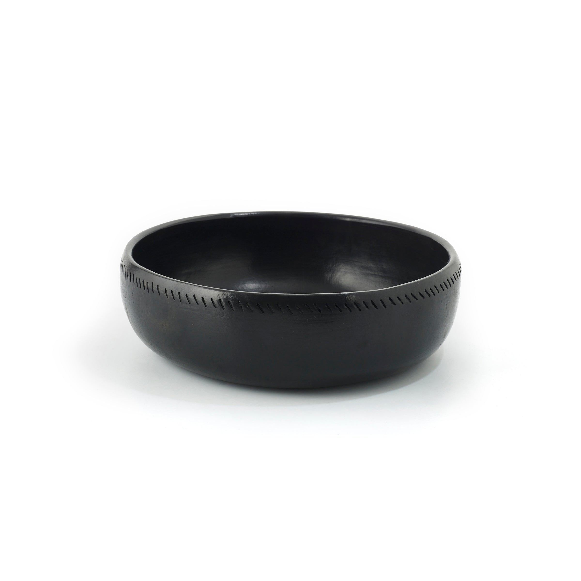 The Barro Bowl by Ames is a handcrafted black ceramic piece featuring a smooth surface and subtle engraved line pattern around the rim. Photographed against a plain white background, it highlights its traditional pottery charm.