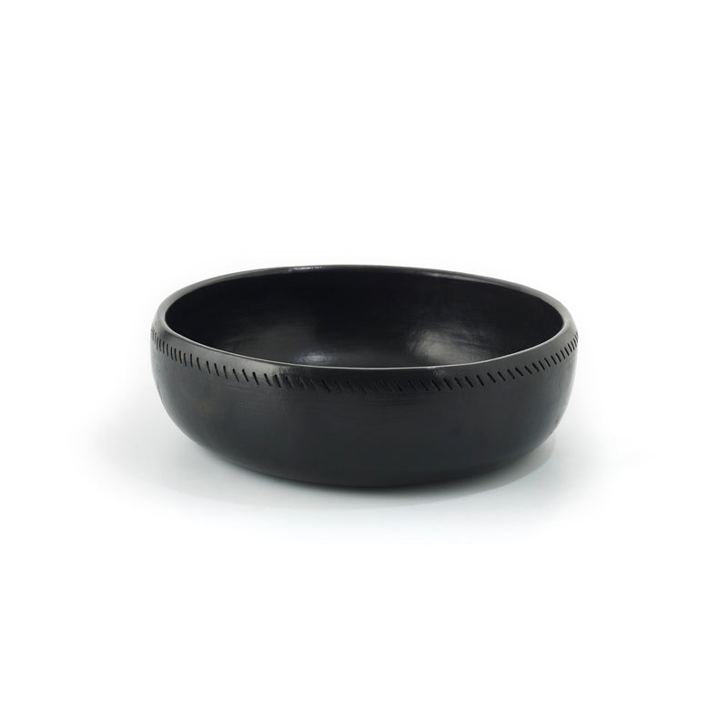 The Barro Bowl by Ames is a handcrafted black ceramic piece featuring a smooth surface and subtle engraved line pattern around the rim. Photographed against a plain white background, it highlights its traditional pottery charm.