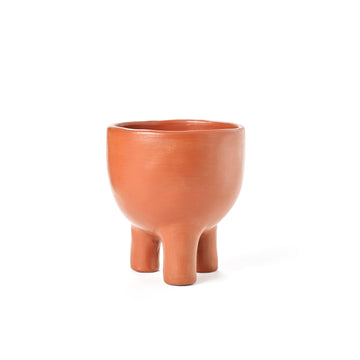 Ames presents the Barro Pot 2, a round terracotta pot featuring a smooth finish and three short, rounded legs. Its minimalist elegance reflects the beauty of Colombian pottery, showcased against a plain white background.