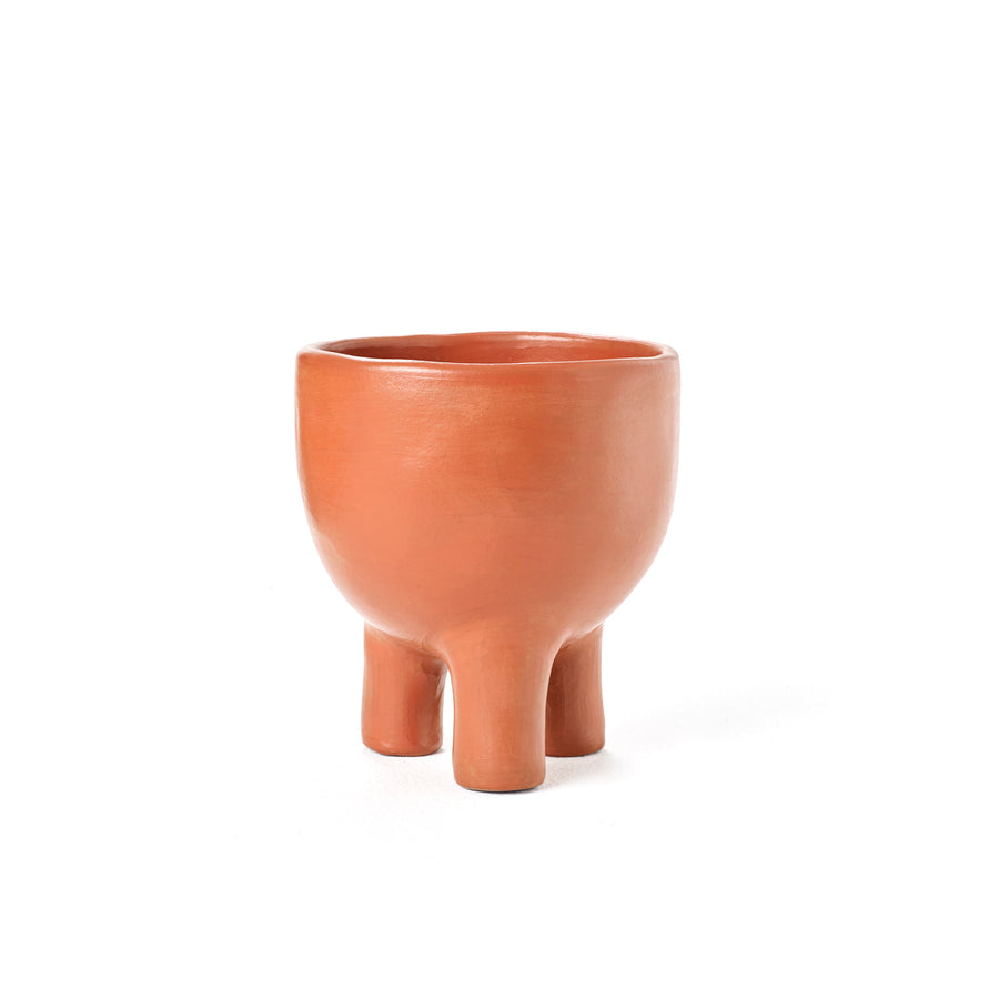 Ames presents the Barro Pot 2, a round terracotta pot featuring a smooth finish and three short, rounded legs. Its minimalist elegance reflects the beauty of Colombian pottery, showcased against a plain white background.