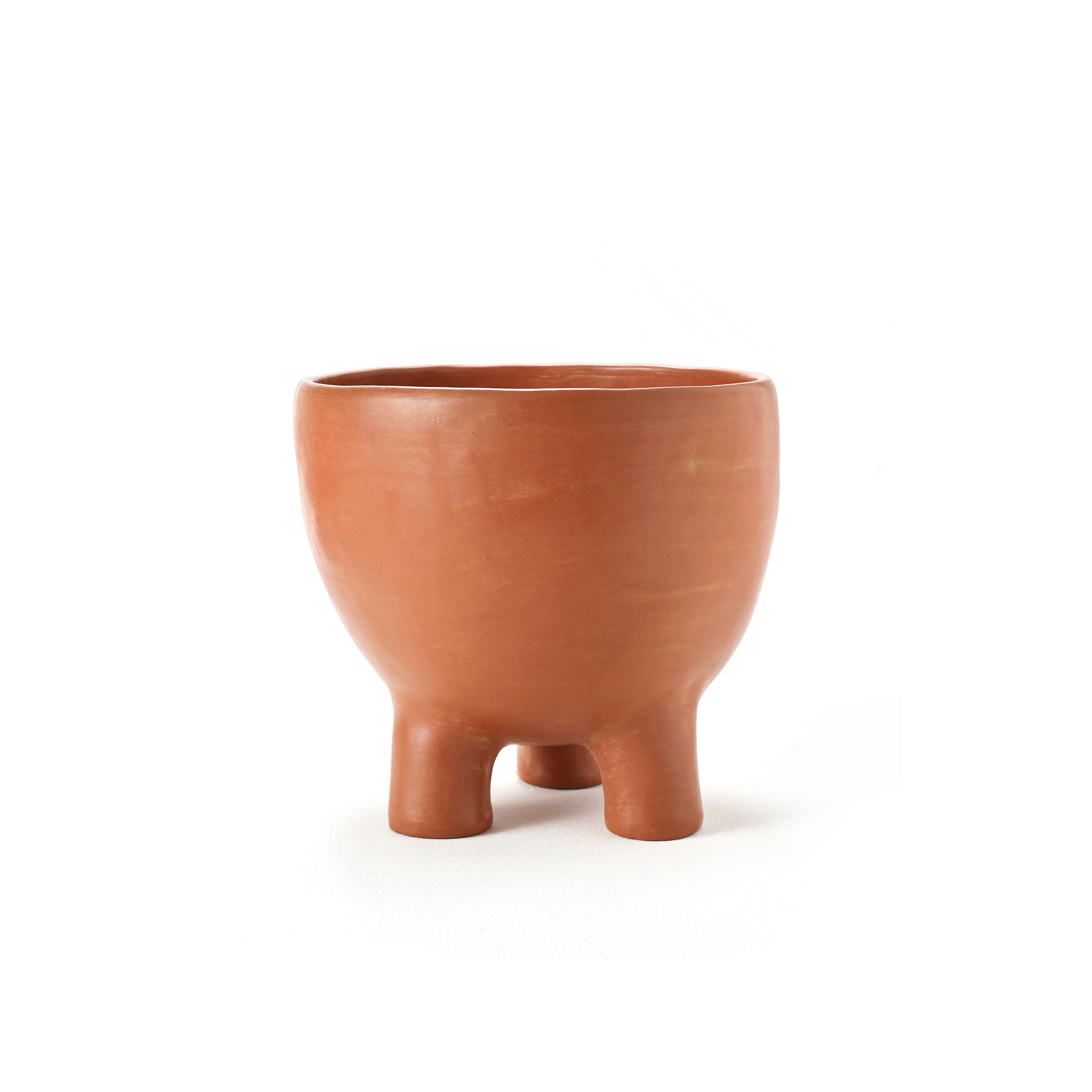 The Barro Pot 2 by Ames is a round terracotta clay bowl with a smooth surface and three short legs, showcased against a plain white background.