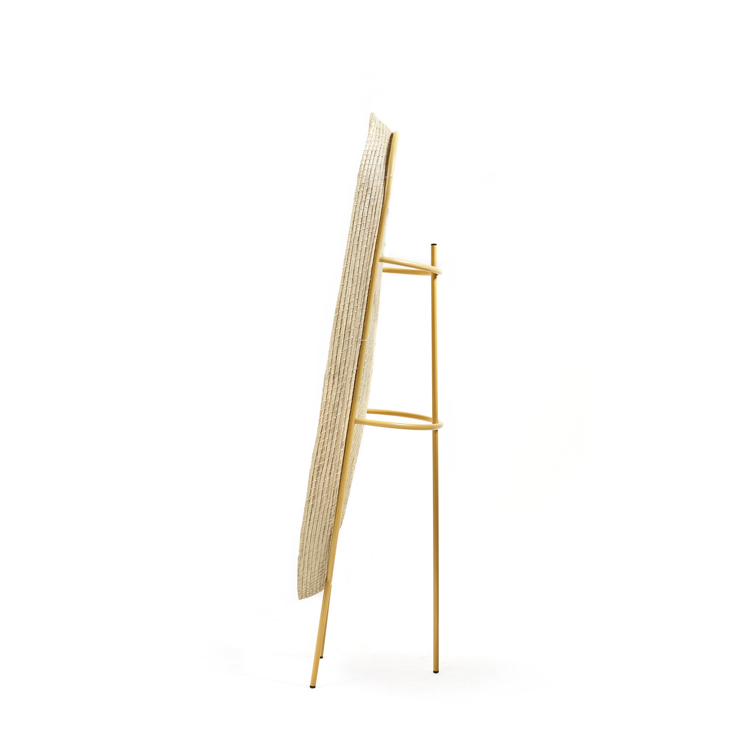 A side view of the Ames Killa Standing Mirror by Ames shows a thin, vertical woven iraca palm panel in a slim yellow metal frame with three legs, set against a plain white background.