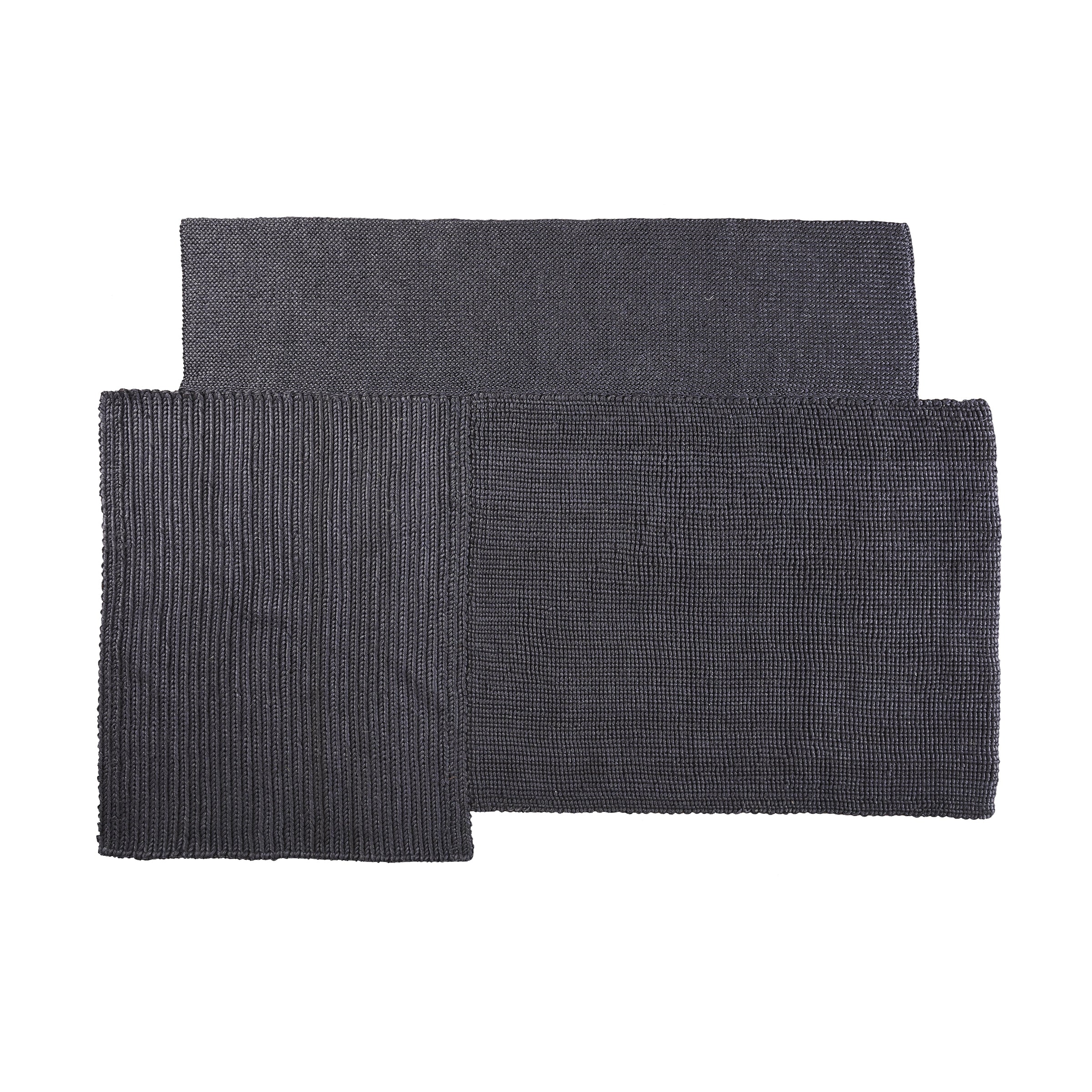 The Cabuya Rug by Ames is a modern, dark grey piece crafted from flame retardant materials. It boasts a textured surface with an overlapping rectangular design and features both ribbed and micro-textured sections, adding minimalist style and a contemporary touch to any interior space.