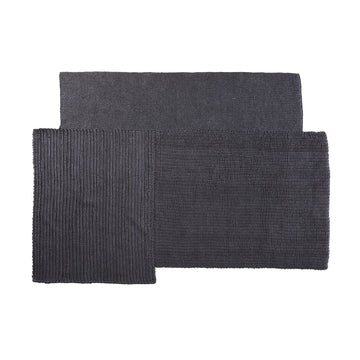 The Cabuya Rug by Ames is a modern, dark grey piece crafted from flame retardant materials. It boasts a textured surface with an overlapping rectangular design and features both ribbed and micro-textured sections, adding minimalist style and a contemporary touch to any interior space.