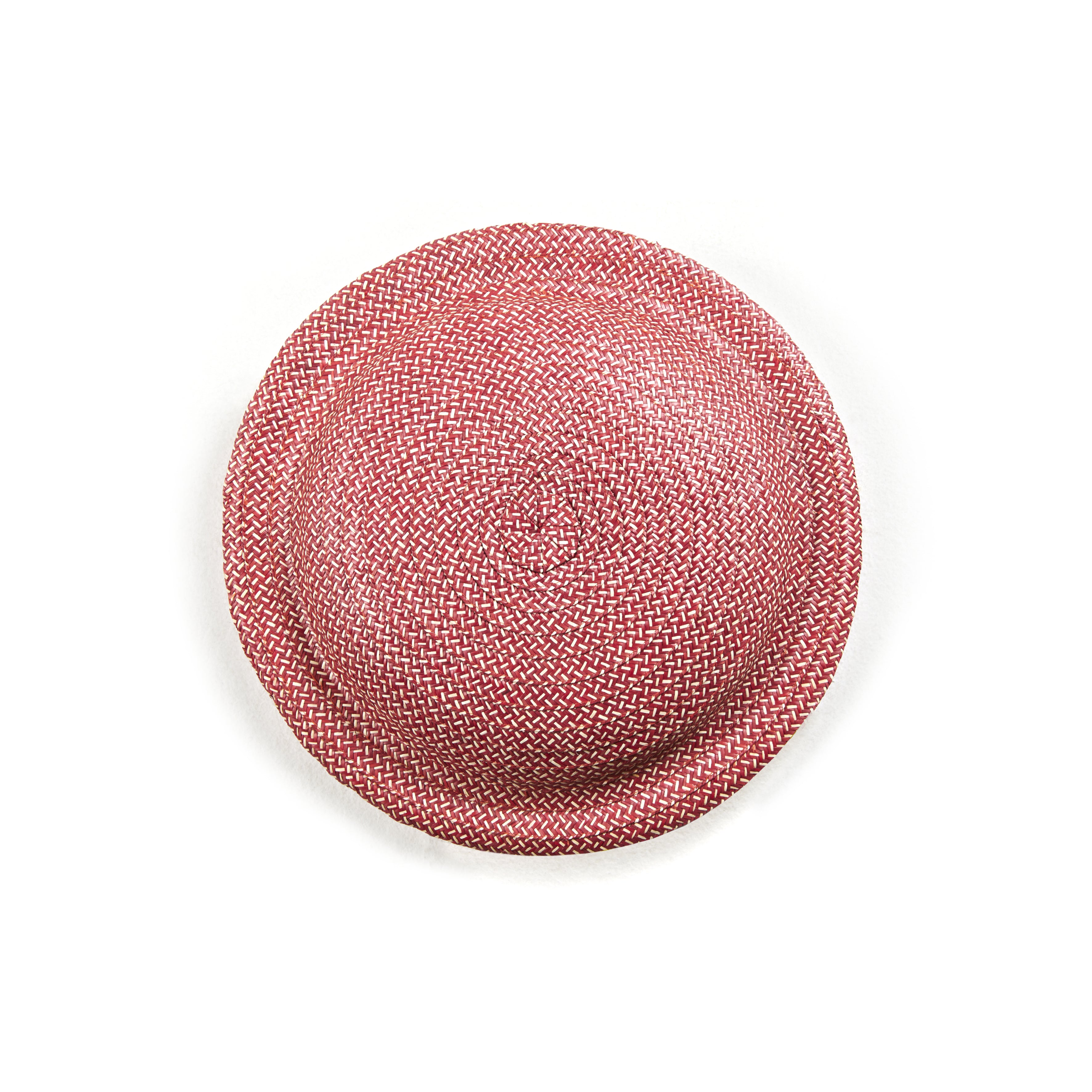 On a plain white background, the Cana Stool by Ames features vibrant colors similar to a round, textured pink woven straw hat with a flat brim and slightly elevated crown.
