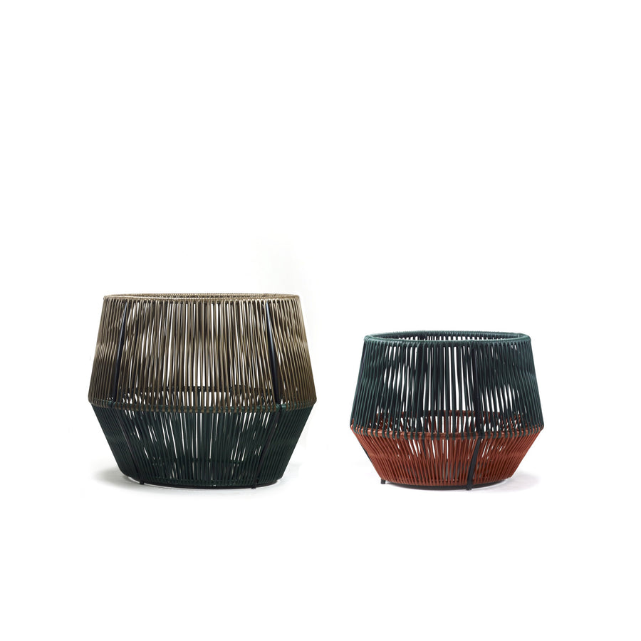 Two geometric Caribe Chic Basket 2 by Ames on a white background. The larger basket has dark green and brown hues, and the smaller one has dark green and rust orange tones. Both feature an angular design with vertical slats made from recycled plastic using the mamposino braiding technique.