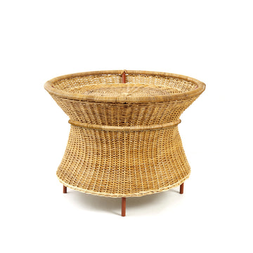 The Ames Caribe Natural Basket Table by Ames features a flared base and woven rattan design, capturing natural wicker elegance in the spirit of Sebastian Herkner. It stands on short wooden legs against a plain white background.
