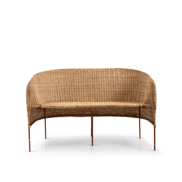 The Caribe Natural Sofa by Ames features a natural-colored, woven rattan design with a curved backrest and slim metal legs, showcasing exquisite Colombian craftsmanship against a plain white background.