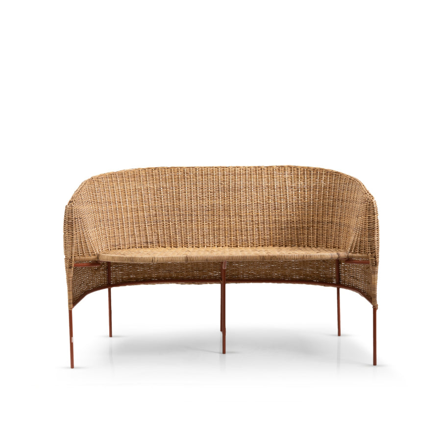 The Caribe Natural Sofa by Ames features a natural-colored, woven rattan design with a curved backrest and slim metal legs, showcasing exquisite Colombian craftsmanship against a plain white background.