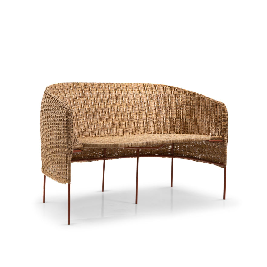 The Caribe Natural Sofa by Ames is a woven rattan two-seater with Colombian craftsmanship, featuring a curved backrest and slender metal legs against a white background.
