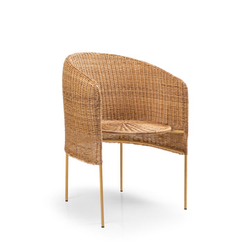 The Ames Caribe Natural Dining Chair by Ames showcases Colombian craftsmanship with a rounded backrest, armrests, woven rattan seat, and slim gold metal legs, set against a plain white background.