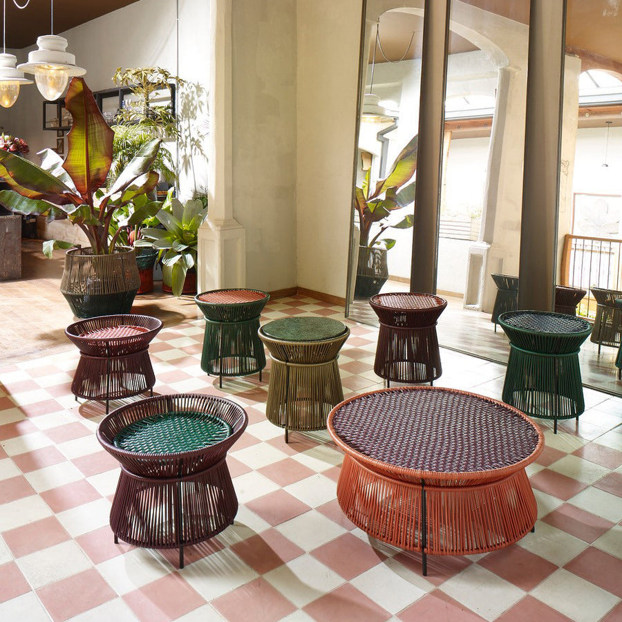 A stylish room with pink and white checkered floors, featuring Ames Caribe Chic Low Tables by Ames, plus round stools, large potted plants, and a wall-sized mirror.
