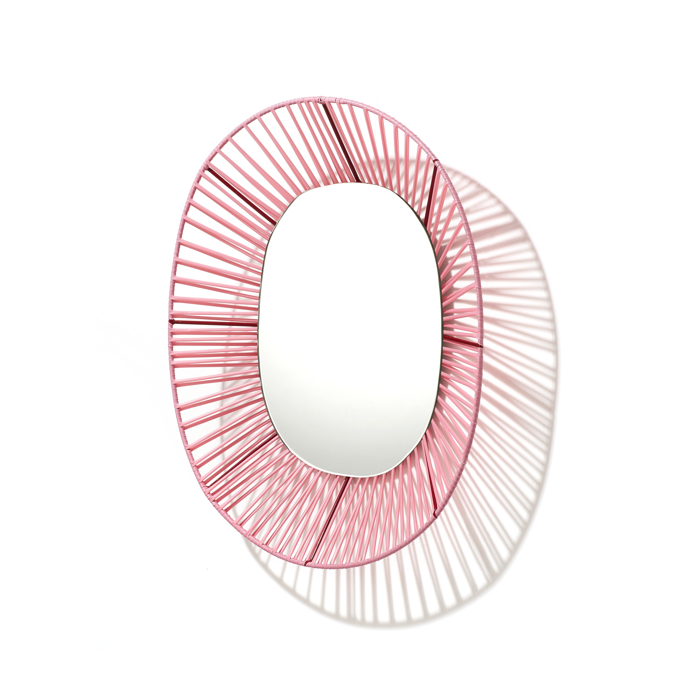 The Cesta Mirror from Ames features a vibrant pink wireframe design crafted from recycled PVC, creating intricate shadows on a white backdrop.