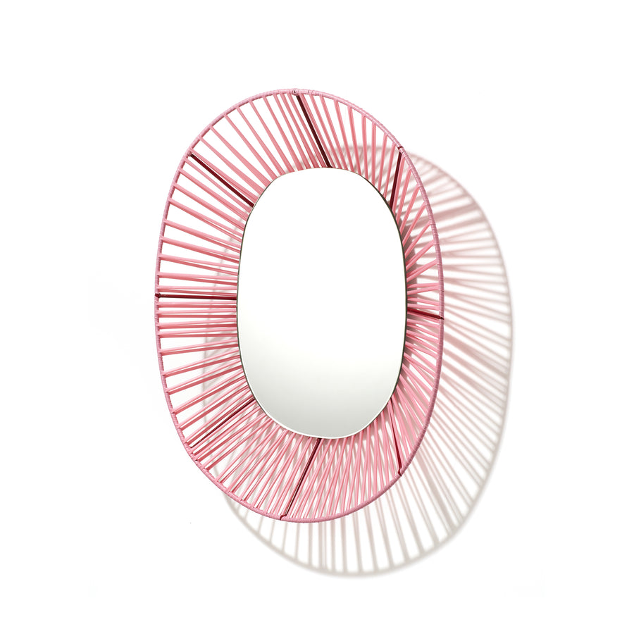 The Cesta Mirror from Ames features a vibrant pink wireframe design crafted from recycled PVC, creating intricate shadows on a white backdrop.