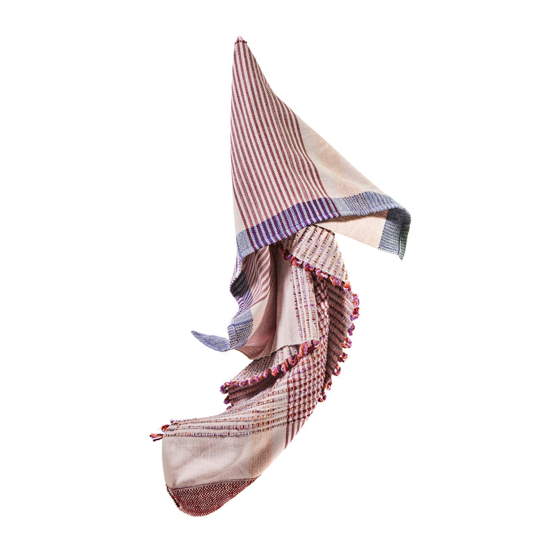 The Ames Chumbes Throws, designed by Mae Engelgeer, exhibit a multicolored plaid pattern with red, blue, and cream stripes and checks. Featuring soft folds against a white background, the edges are adorned with small tassels.