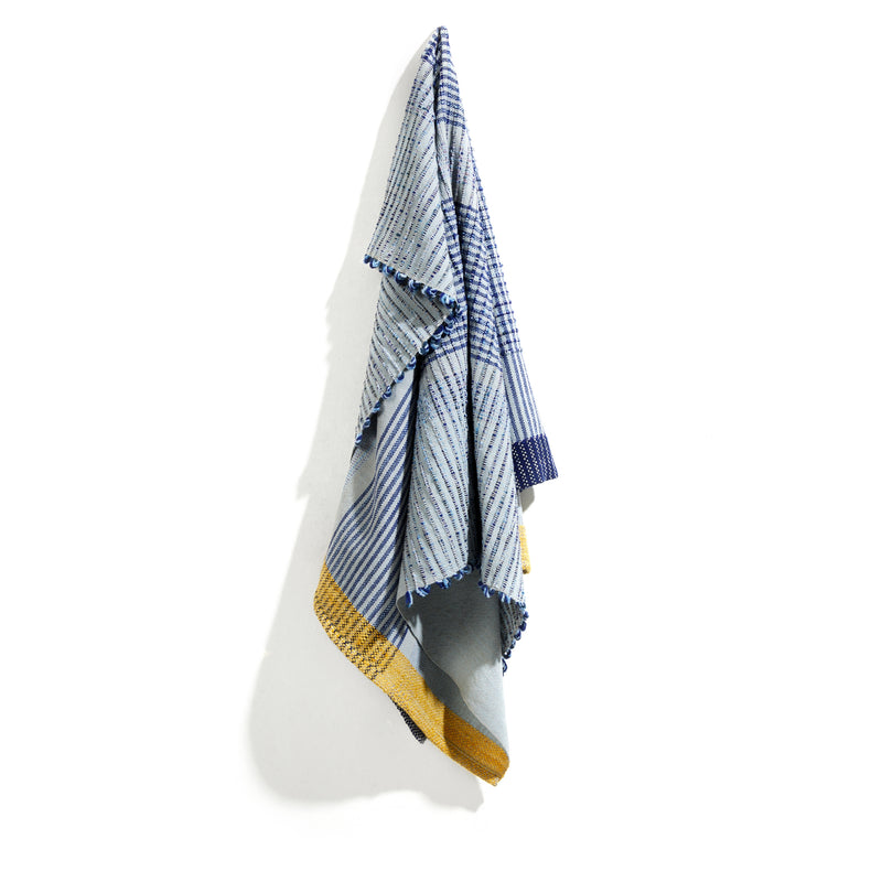Ames Chumbes Throws, featuring a blue and white plaid pattern with yellow trim, hangs elegantly against a plain white background.