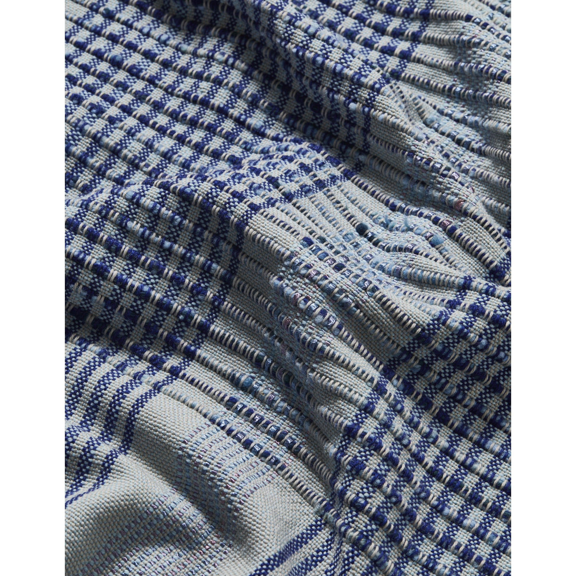 A close-up of Ames Chumbes Throws reveals a textured blue and white plaid design with alternating squares of tight and loose weaves, creating a varied surface. This intricate hand-woven pattern is something Mae Engelgeer would admire for its unique shades.