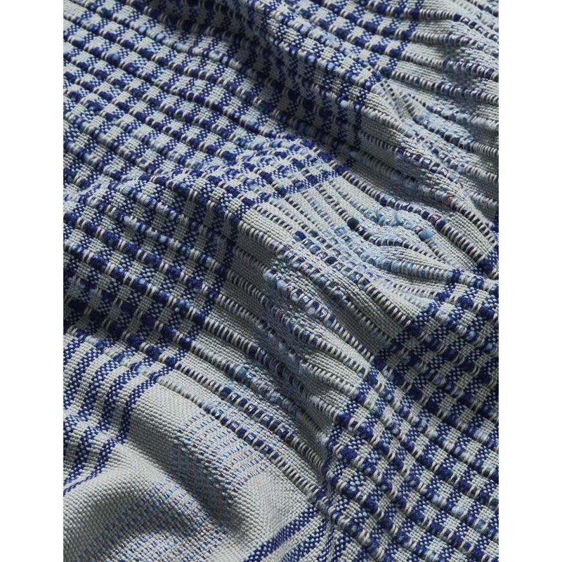 A close-up of Ames Chumbes Throws reveals a textured blue and white plaid design with alternating squares of tight and loose weaves, creating a varied surface. This intricate hand-woven pattern is something Mae Engelgeer would admire for its unique shades.