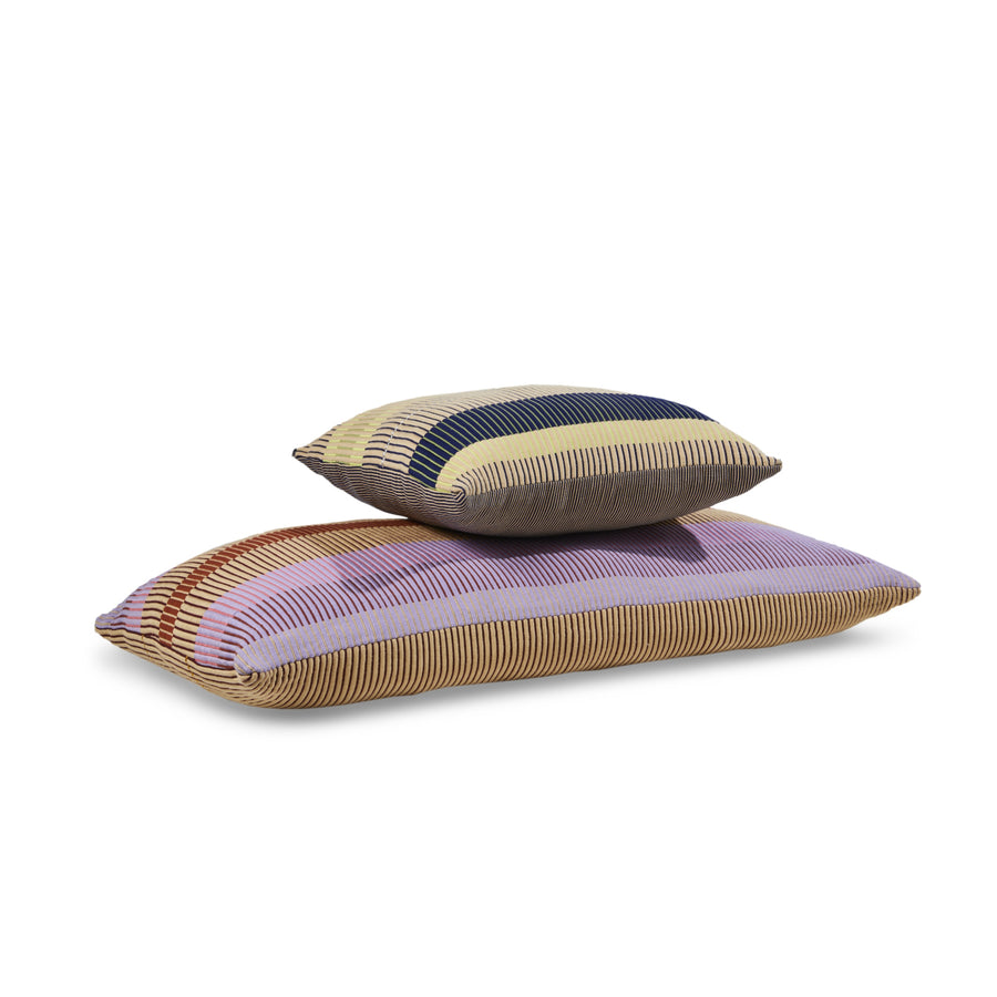 Two Chumbes Layer rectangular pillows by Ames are stacked, showcasing hand-woven striped patterns in purple, beige, blue, and brown. These cushions create a textured look with their varying colors against a plain white surface.